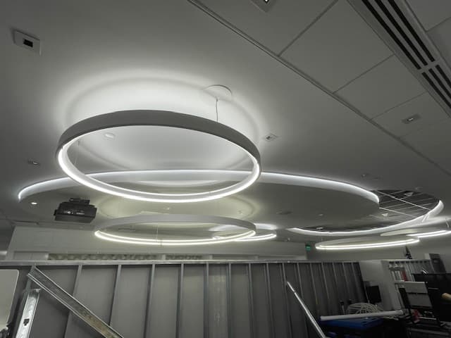 Large circular LED light fixtures suspended from a white ceiling above metal wall framing.